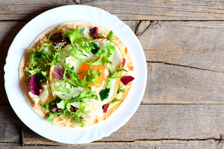Fried egg, salad mix, hummus, fresh parsley on a tortilla. Homemade tortilla on a plate isolated on old wooden background with copy space for text. Yummy and quick breakfast. Top viewの写真素材