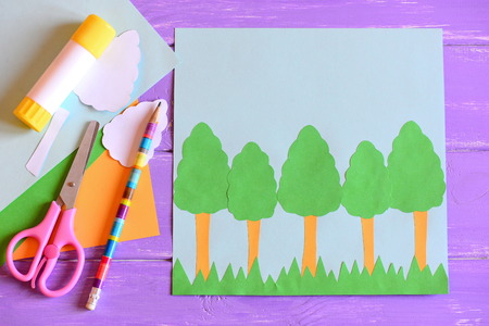 Making Earth day card. Step. Guide. Earth day card with trees and grass, scissors, glue stick, pencil, template, paper sheets on a wooden table. Earth day paper crafts project for children. Top viewの写真素材