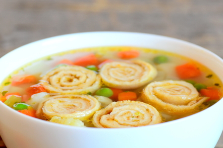 Vegetable soup with omelet rolls in a bowl on rustic wooden table. Diet soup with omelet, carrot, peas, leek, cauliflower and potatoes. Closeupの写真素材