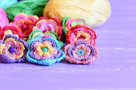 Crochet flowers embellished with buttons and beads. Beautiful crochet flowers, colored cotton yarn on purple wooden table. Easy summer floral crafts. Closeupの写真素材