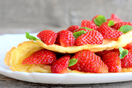 Delicious berry egg omelette. Home omelette stuffed with juicy strawberries and garnished with mint leaves on a plate and a wooden table. Healthy breakfast or brunch for kids and whole family. Closeupの写真素材