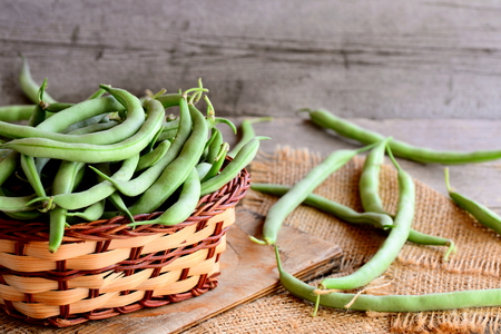 Long green beans in a brown wicker basket on a wooden board and a burlap textile. Vintage wooden backgroundの写真素材