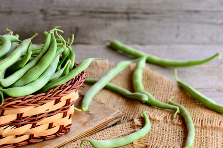 Fresh green beans in a brown wicker basket on a wooden board and a burlap textile. Rustic wooden backgroundの写真素材