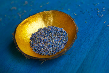 Lavender seeds in handmade coconut bowl decorate with gold from the inside on blue wooden background. Space for text.の写真素材