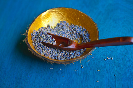 Lavender seeds in handmade coconut bowl decorate with gold from the inside and a wooden spoon on blue wooden backgroundの写真素材