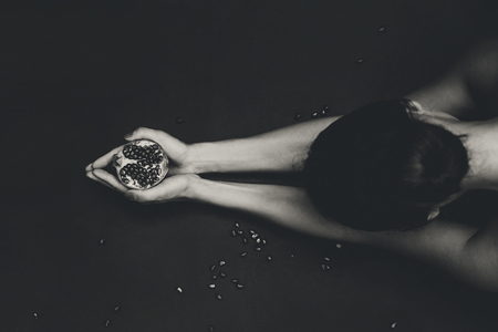 close up of attractive young woman with pomegranate at black backgroundの写真素材