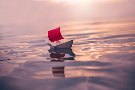 paper boat with red sail floating on waterの写真素材