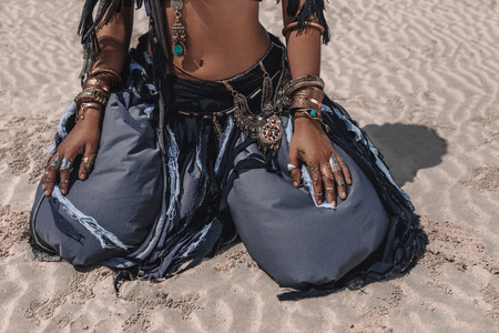 close up of beautiful young stylish tribal dancer in oriental costume sitting on sand outdoorsの写真素材