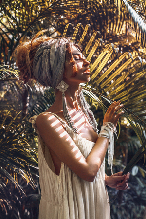 beautiful young fashionable woman in turban posing at natural tropical backgroundの写真素材