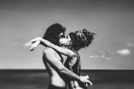young couple hugging and kissing through the face masks on the beachの写真素材