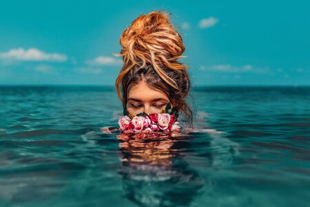 beautiful young woman swimming in sea with wreath conceptual fashion portrait の写真素材