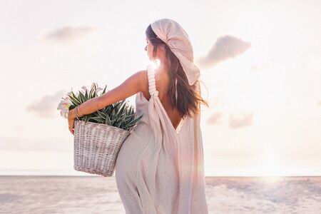 beautiful young stylish woman with basket with flowers outdoors at sunsetの写真素材