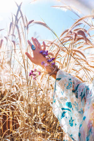 stylish woman hand with ring anf flowers on the field in summer sun lightの写真素材