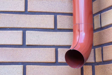 Brown gutter pipe against a brick wall background.の写真素材
