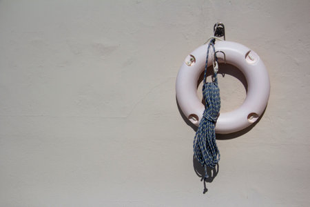 Lifebuoy with rope on white wall. Place for text.