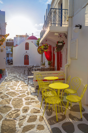 Mykonos streetview at sunrise with chapel and yellow chairs and tables, Greeceの写真素材