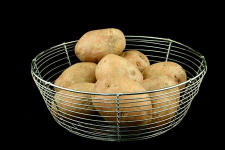Some red potatoes put in a wire bowl on the black backroundの写真素材