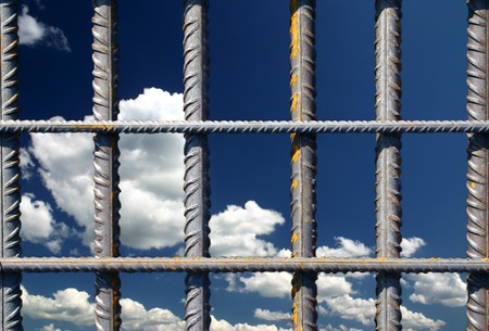 View at steel bars on a blue sky background which looks like iron bars in a prison