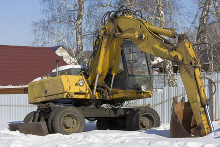 Wheeled excavator stands under the open sky in the yard in winter.