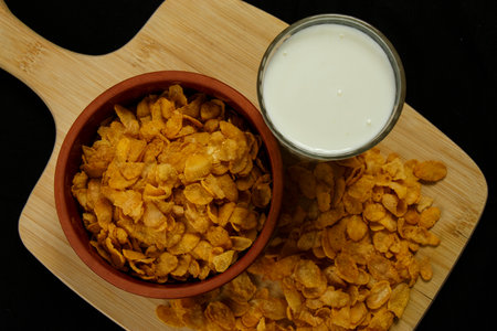 <p>A bowl of cornflakes and a glass of milk on the kitchen board high-angle shot Black Background</p>の写真素材