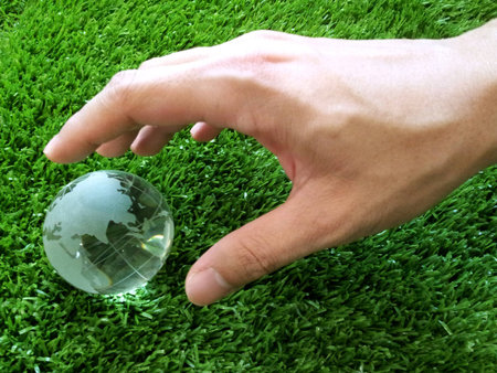 Male hand reaching out for glass globe on grass background.の素材