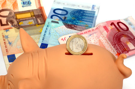 Pink piggy bank with a coin and bills in the backgroundの写真素材