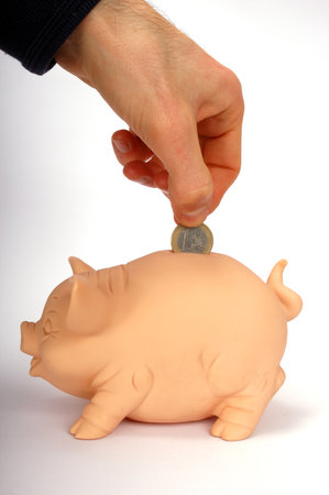 Hand putting a coin in a pink piggy bank with a neutral backgroundの写真素材