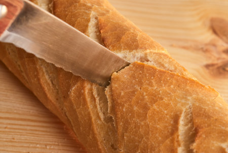 Cutting a loaf of bread with a knife on a wooden boardの写真素材