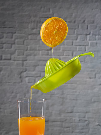 Juice falling from half an orange into a juicer, which is filling a glass