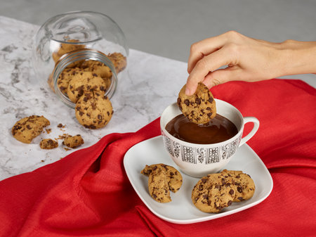 Hand picking up a chocolate cookie and cup with hot chocolateの写真素材
