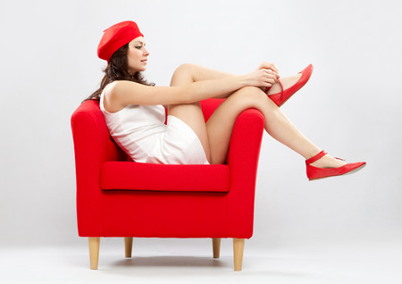Beautiful smiling woman relaxed on red armchair isolated on greyの写真素材