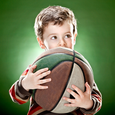 cute child hold big basket ball on green backgroundの写真素材