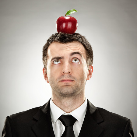 surprised businessman red apple on head on grey backgroundの写真素材