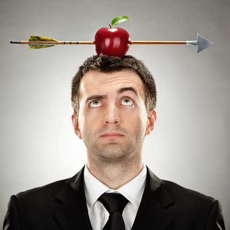 surprised businessman red apple on head hit by arrow on grey backgroundの写真素材