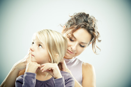 Beautiful brunette woman with young blond girl on grey backgroundの写真素材