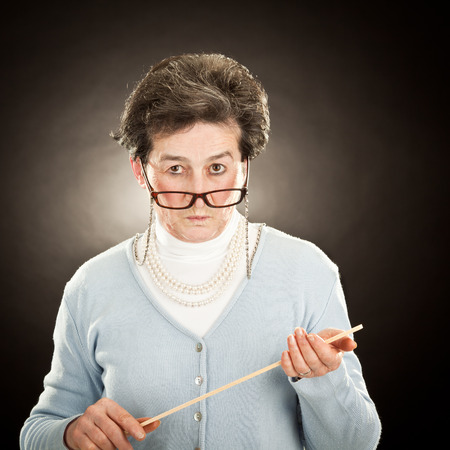 old strict teacher with glasses isolated on blackの写真素材