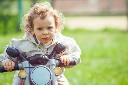 beautiful blond curly hair child play with bike outdoor in a parkの写真素材