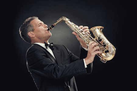 handsome businessman play saxophone isolated on blackの写真素材