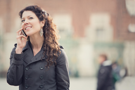 smiling curly woman talking on phone in cityscapeの写真素材
