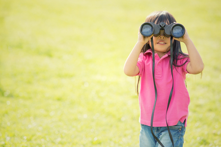 happy asian smiling child play with binoculars in a gardenの写真素材