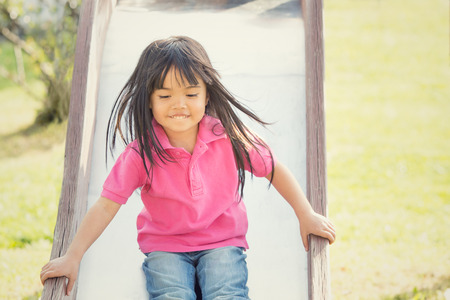 happy asian smiling child play with slide in a parkの写真素材