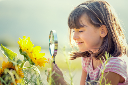 smiling child playing with magnifying glass in a gardenの写真素材