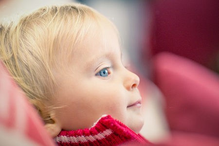 Little blond blue eyes girl with red sweater at homeの写真素材