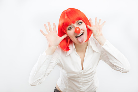 pretty young brunette caucasian woman with red nose and wig making a face on white backgroundの写真素材