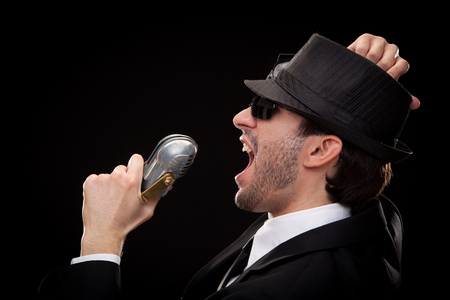 elegant man singer musician singing to microphone isolated on blackの写真素材