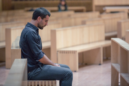 Young beard man wearing blue shirt praying in modern churchの写真素材