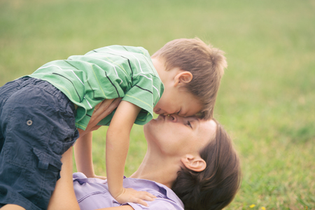 happy blond caucasian kid outdoor family portrait at park kissed by his mumの写真素材