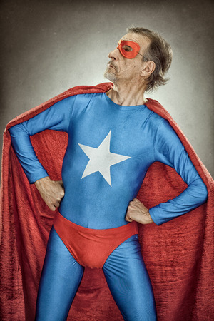 senior superhero man in blue costume red cloak and mask old portrait on textured backgroundの写真素材