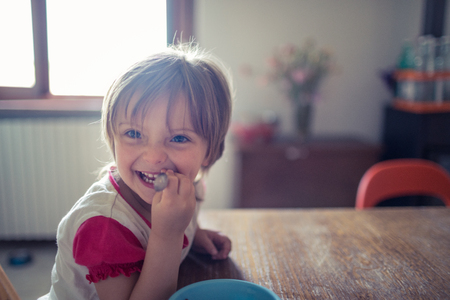 Happy blonde girl daughter with blue eyes smiling while playing on the living room wooden floor. Happy relaxed family life with children at home.の写真素材