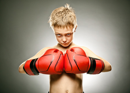 young angry boy play boxe with gloves portrait on grey backgroundの写真素材